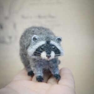 This wool raccoon is 4.5 cm tall and 8 cm long with wired limbs for gentle pose changes. A charming felted forest animal for collectors and woodland displays.