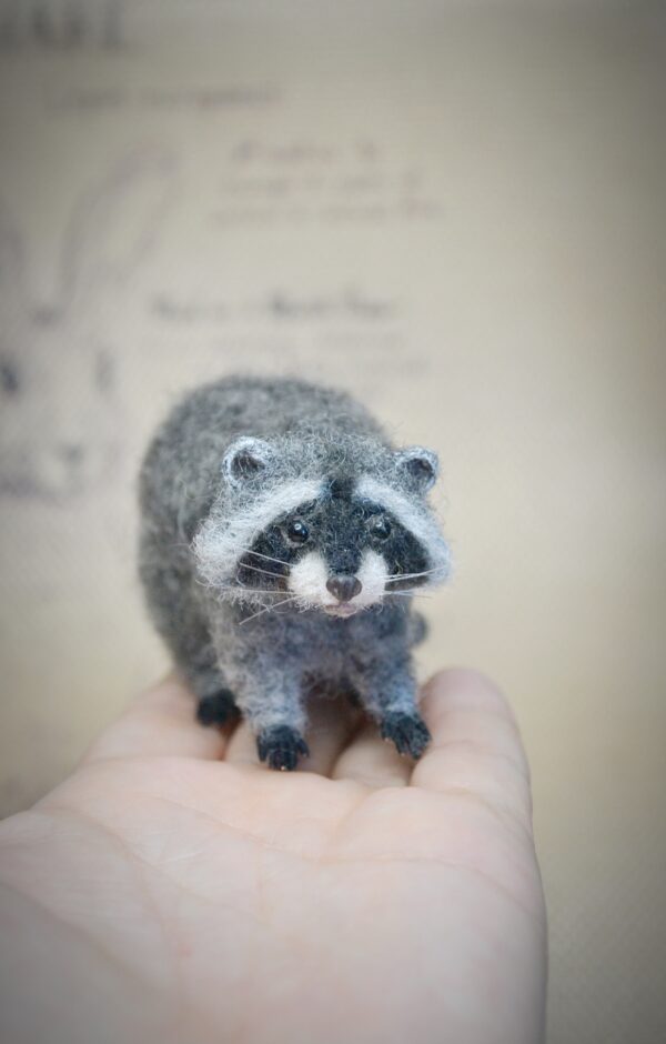 This wool raccoon is 4.5 cm tall and 8 cm long with wired limbs for gentle pose changes. A charming felted forest animal for collectors and woodland displays.