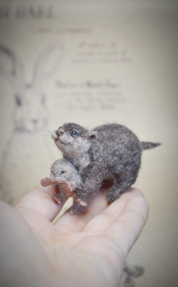 This needle felted otter holds a tiny baby, which can be displayed separately. Wire in the limbs allows gentle pose changes — a perfect river scene in miniature.