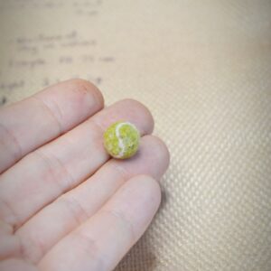 Miniature wool tennis ball, handmade with curved white lines. A tiny felted accessory for dollhouses, pets, or sports-themed mini scenes.