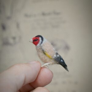 This 2.5 cm goldfinch bird is handmade from wool with realistic red, black, and gold markings. A soft sculpture for miniature scenes and bird lovers.