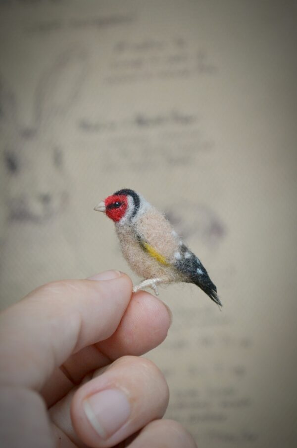 This 2.5 cm goldfinch bird is handmade from wool with realistic red, black, and gold markings. A soft sculpture for miniature scenes and bird lovers.